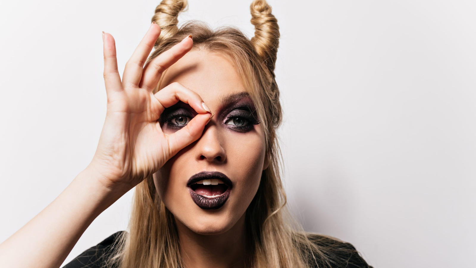 Attractive little witch posing in studio. Inspired blonde woman preparing for carnival party.