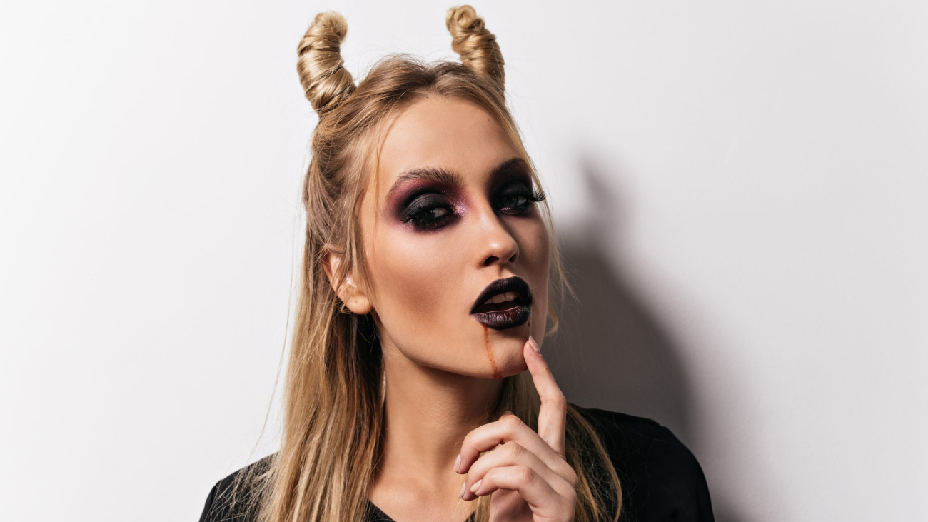 Close-up shot of beautiful vampire. Indoor photo of lady with scary makeup posing in halloween.