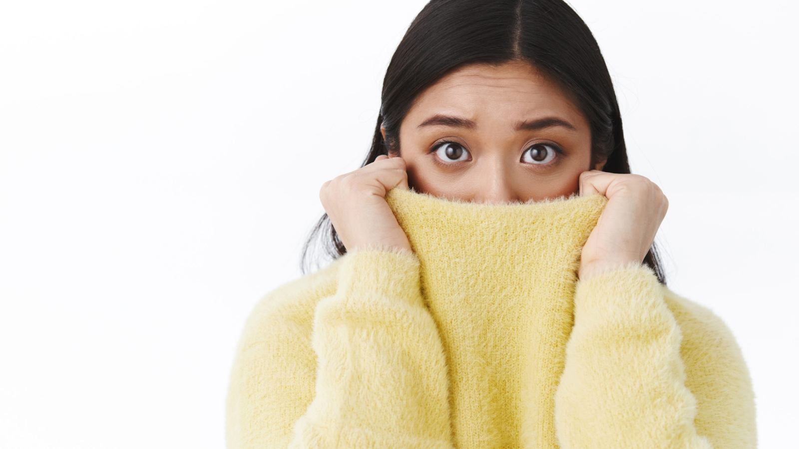 Close-up portrait timid and insecure cute asian girl pull sweater collar on face as feel afraid and scared of horror movie, eyes exress fear, trembling frightened, standing white background.